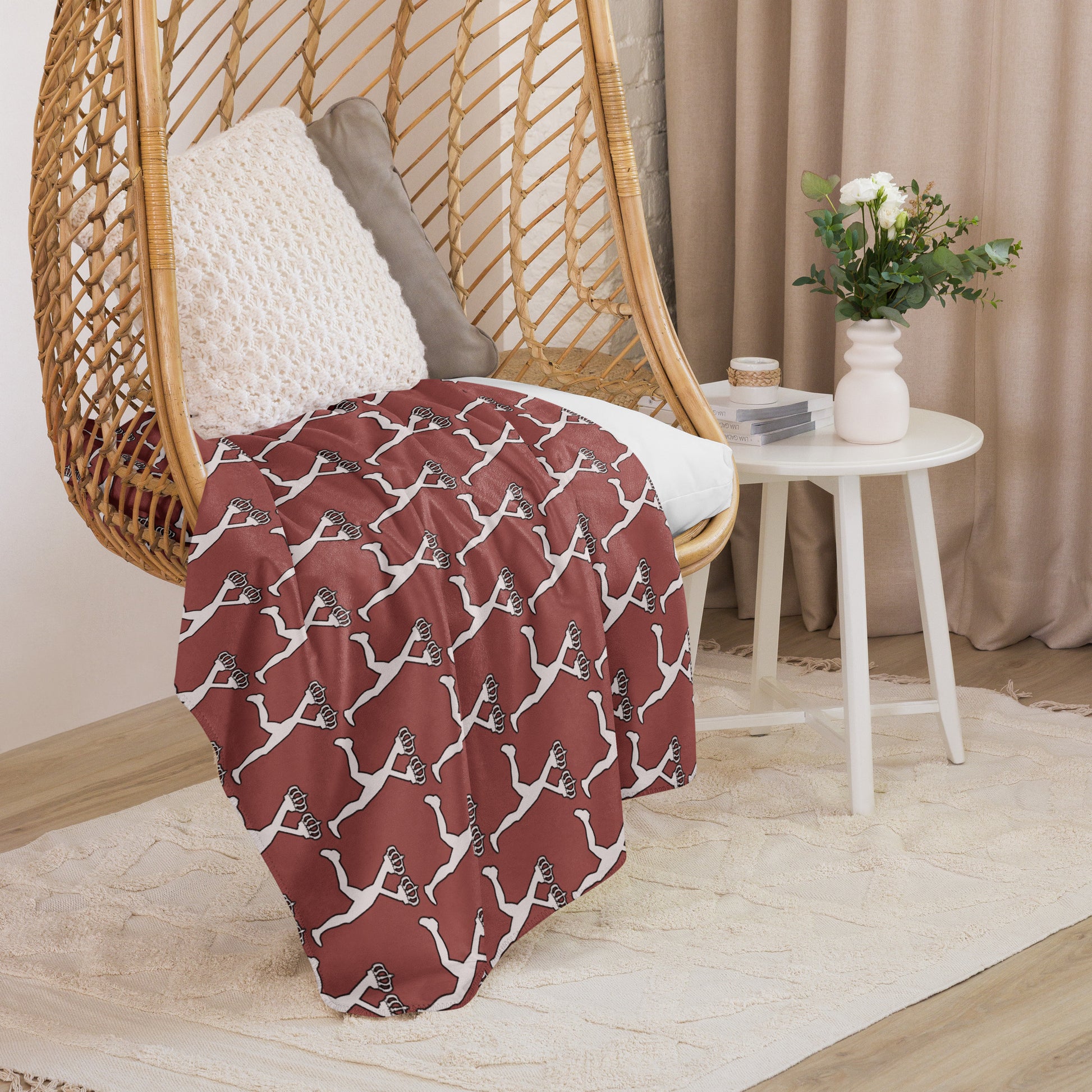 Red sherpa blanket with white Lux mascot pattern draped over a wicker chair in a cozy room.