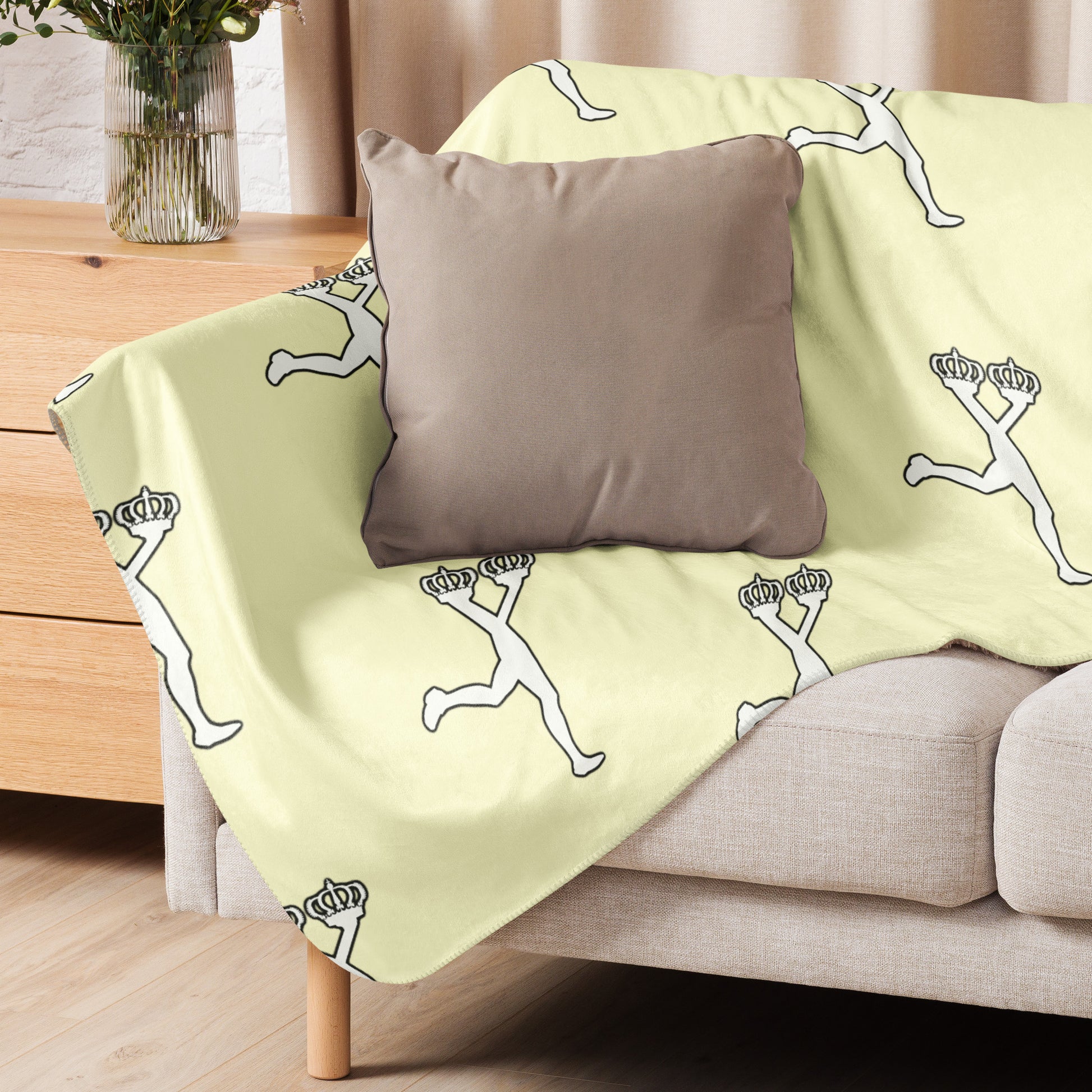 Cream blanket with white graphics of the iconic Lux mascot draped over a beige sofa with a brown pillow.