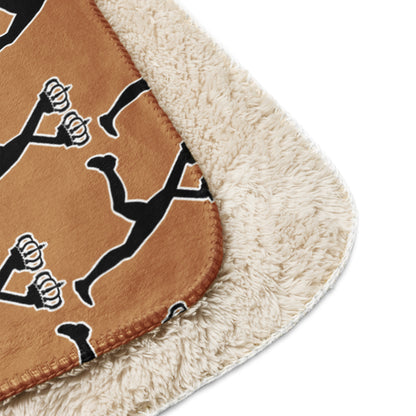 Close-up of a brown throw  sherpa blanket with black and white designs of Lux with the iconic two crowns on a beige border.
